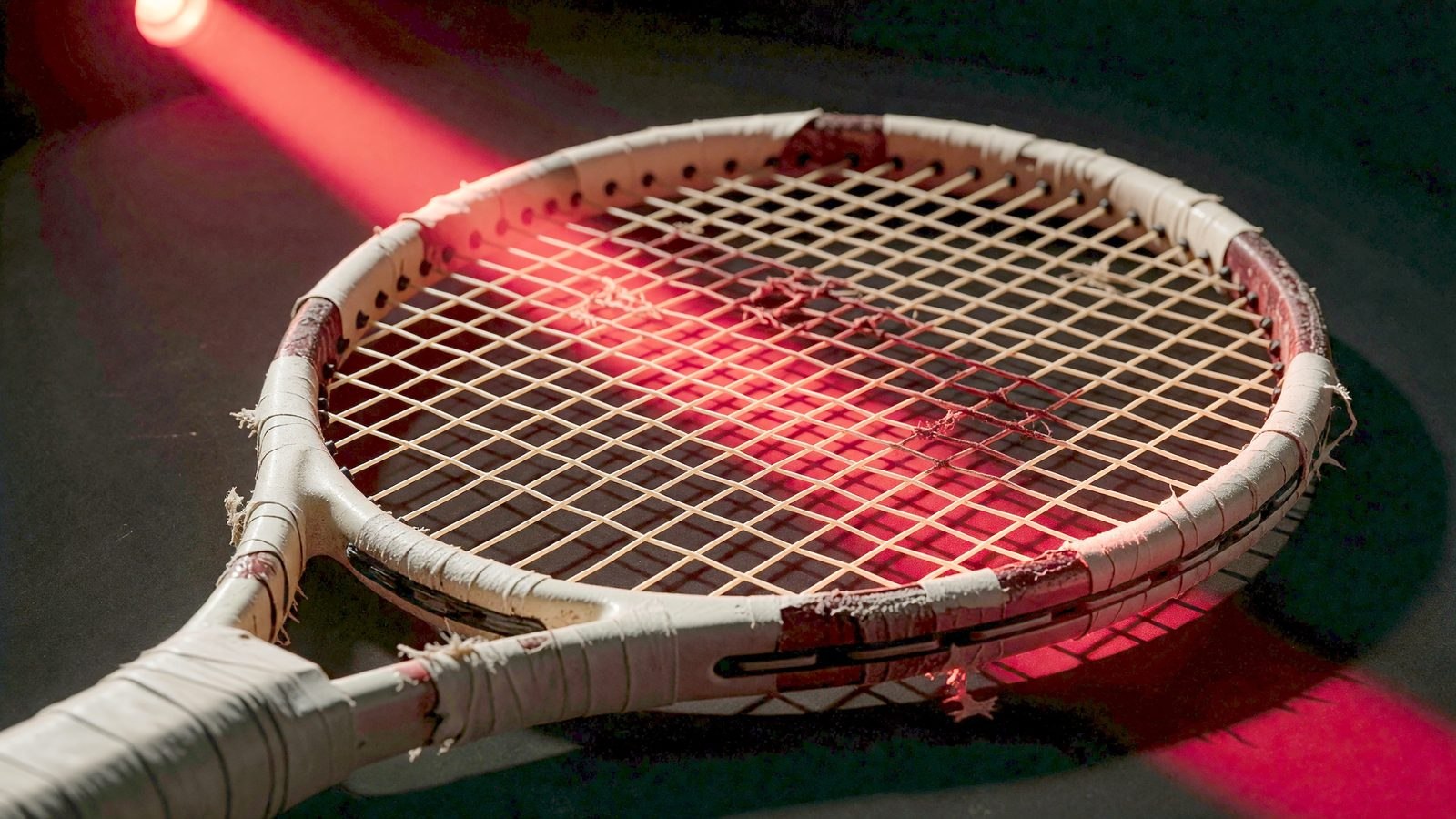 Gros plan sur les cordes tendues d'une raquette de tennis éclairées d'une lumière rouge dramatique