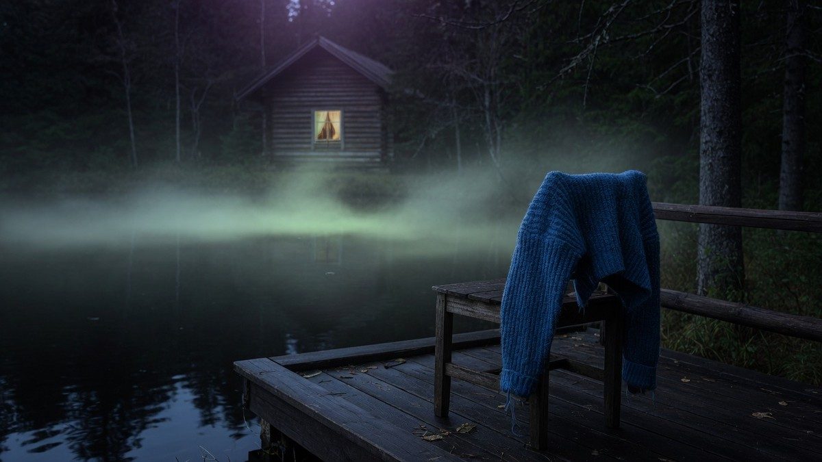 Chalet isolé au bord d'un lac dans la brume nocturne, avec un pull bleu posé sur une véranda en bois