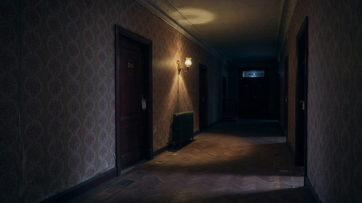 Couloir sombre et désert d'un vieil hôtel éclairé par une seule applique murale, ambiance mystérieuse