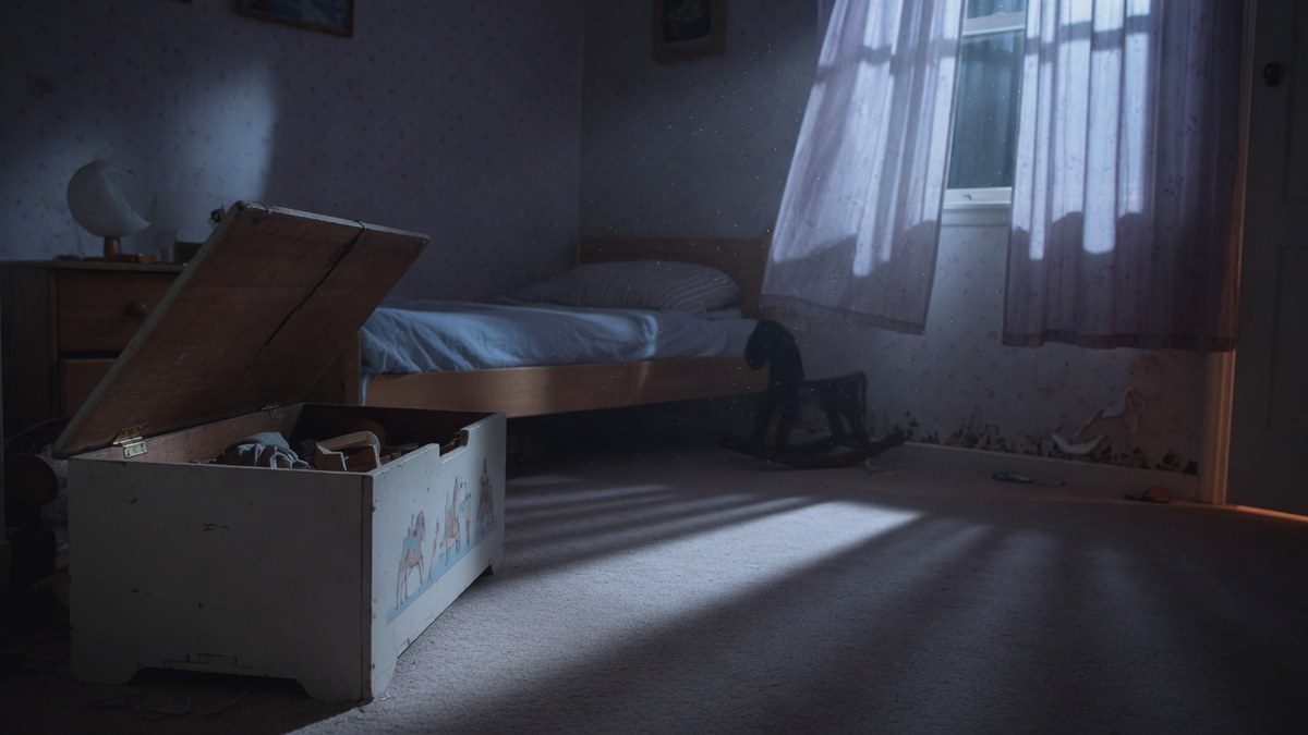 Chambre d'enfant la nuit vue au ras du sol, coffre à jouets entrouvert, clair de lune à travers les rideaux.