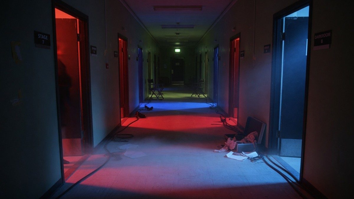 Couloir de studio de tournage plongé dans une lumière rouge et bleue inquiétante, sans personnage visible