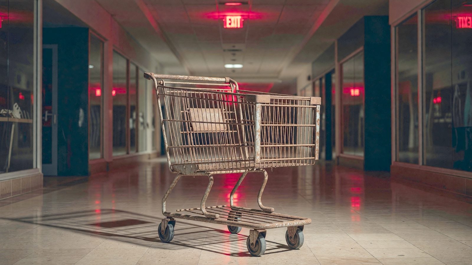 Un chariot de supermarché abandonné dans un couloir de centre commercial désert, éclairé par une lumière d'urgence rouge
