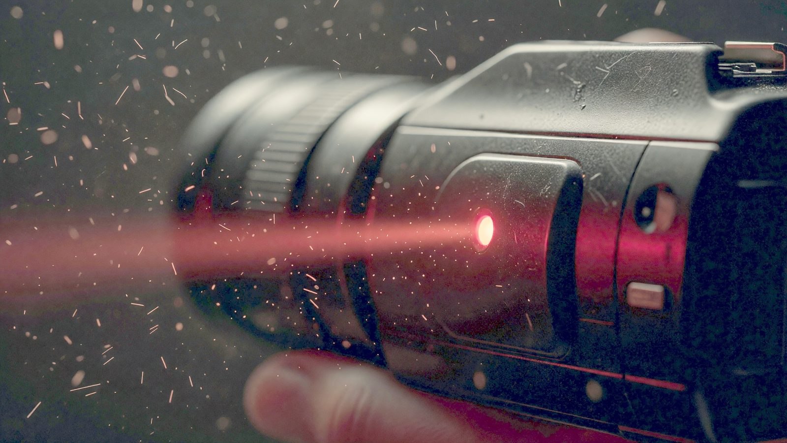 Gros plan sur le voyant d'enregistrement rouge d'une caméra vidéo brillant dans l'obscurité, avec des particules de poussière visibles dans le faisceau de lumière