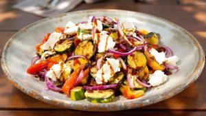 Assiette de salade tiède avec courgettes, poivrons, oignons rouges et mozzarella, nappée de crème de balsamique