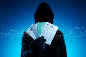 Silhouette d’un hacker tenant un éventail de cartes bancaires, Carte Vitale et documents d’identité sous un éclairage néon bleu vif, illustrant le piratage du fichier FICOBA et l’exposition de 1,2 million de comptes bancaires en France