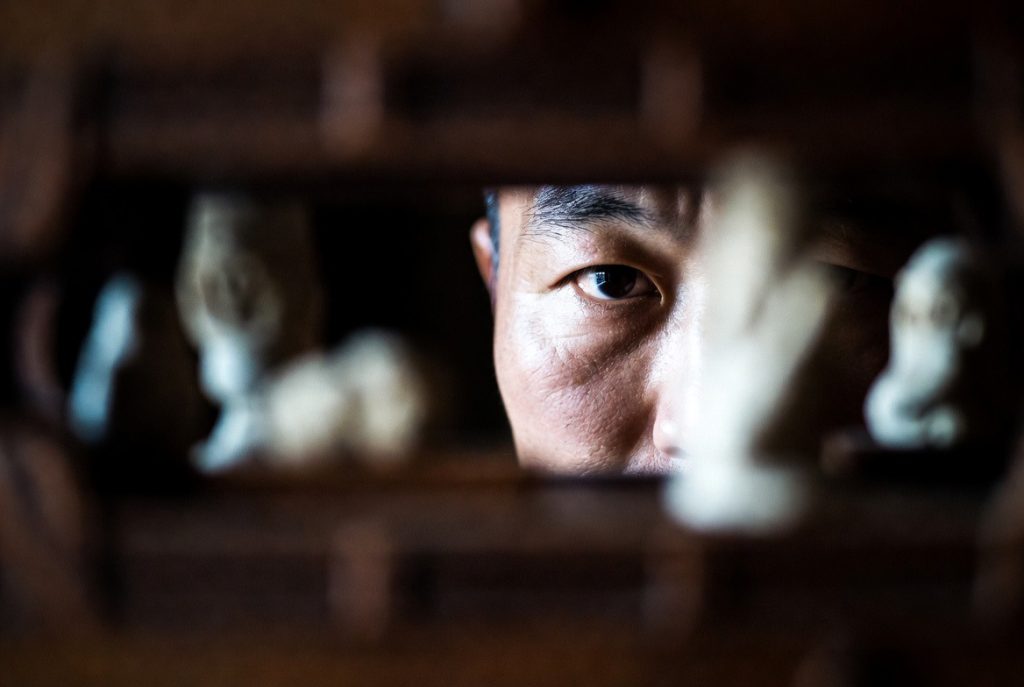 Portrait d’un homme asiatique regardant à travers une ouverture sculptée en bois, expression intense et mélancolique – illustration de The Ugly de Yeon Sang-ho
