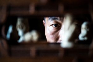 Portrait d’un homme asiatique regardant à travers une ouverture sculptée en bois, expression intense et mélancolique – illustration de The Ugly de Yeon Sang-ho