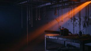 Entrepôt sombre et abandonné avec une tronçonneuse posée dans la pénombre, ambiance inquiétante